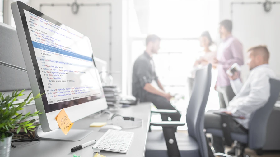 Écran d'ordinateur avec code, personnes discutant en arrière-plan.